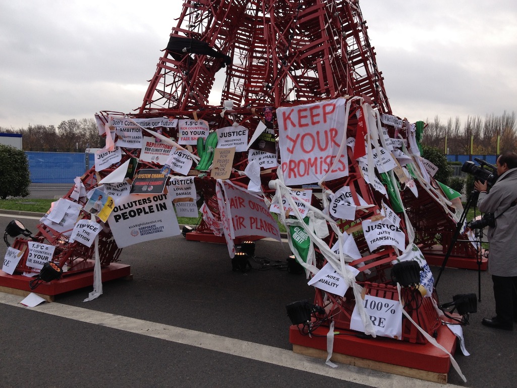Protest signs adorn a mini Eiffel Tower at COP21. Photo: Josha MacNab.
