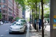 Electric car charging at recharging station in the street under green trees in summertime