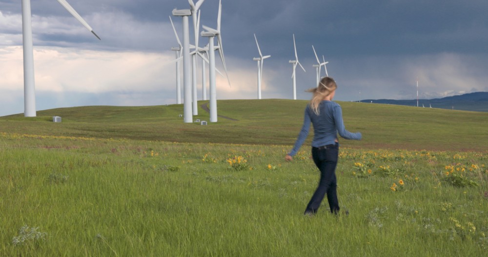 Woman walking in a field with wind turbines in background