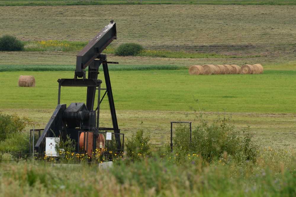 inactive pumpjack in Alberta field with hay bales