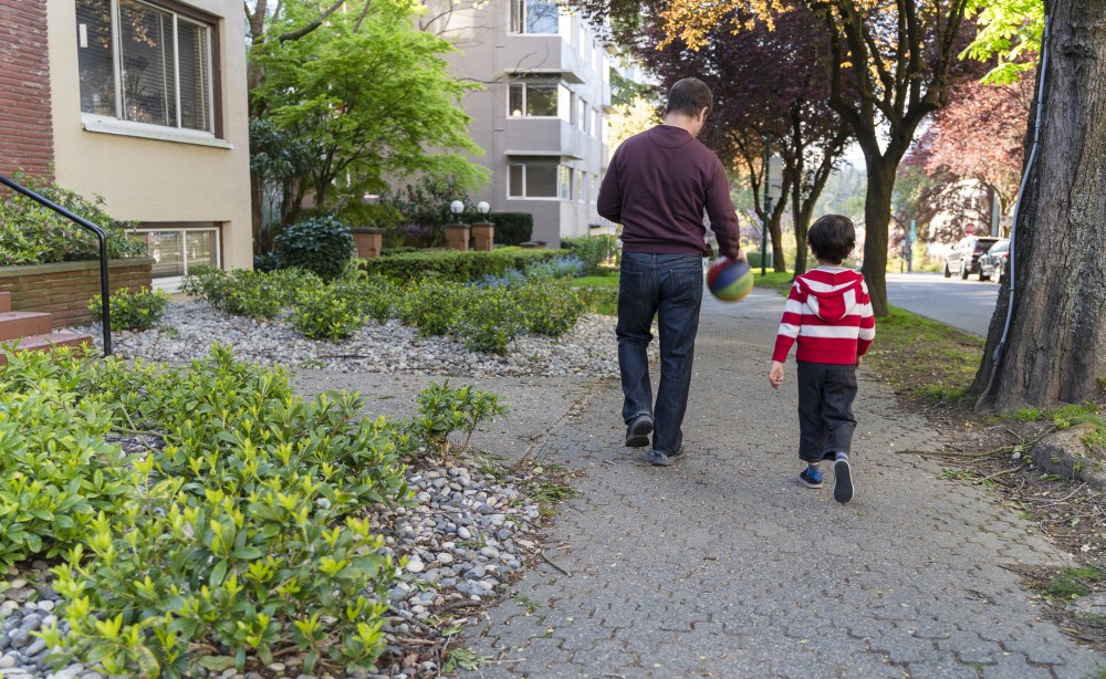 Father and son walking on a BC street next to MURBs