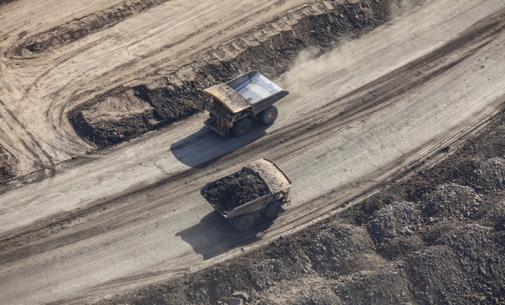 Aerial photo of a large dump trucks driving along a mine road near Fort McMurray, Alberta.