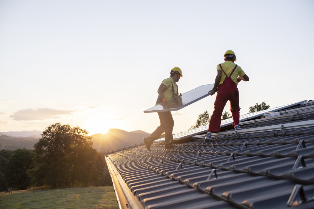 Two engineers on a roof of a building installing solar panels while the sun sets in the background