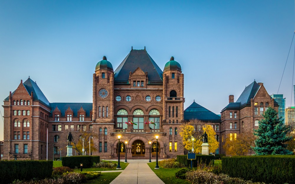 Photo of Ontario Legislature building at dusk with trees changing colours in front