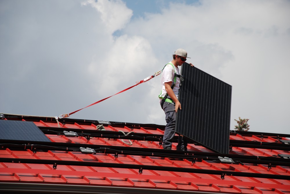 A worker wearing safety gear is secured to a red rooftop while installing solar panel in Edmonton, Alberta