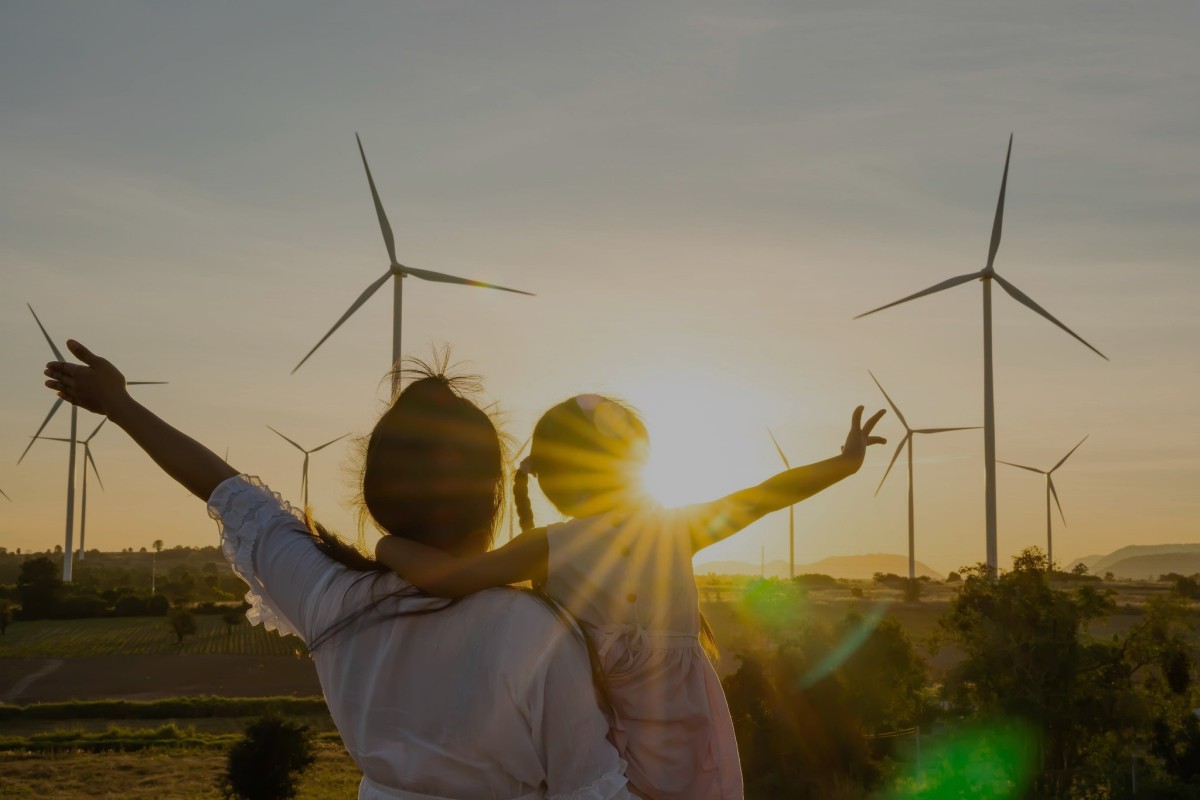 Mother and child in front of wind turbines at sunset.