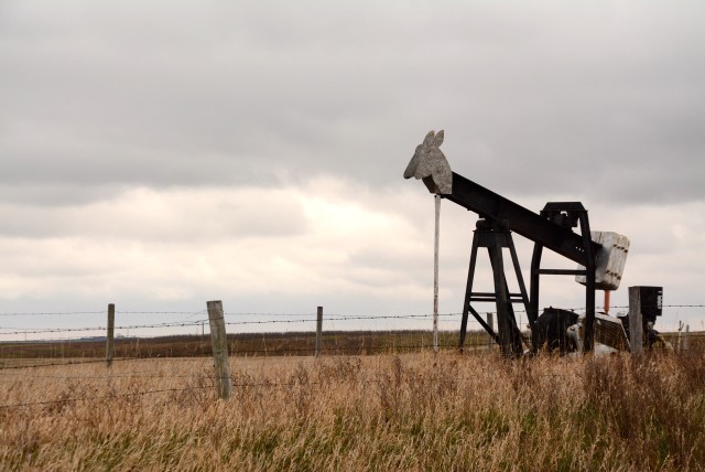 Disabled pumpjack in southern Alberta field under cloudy sky