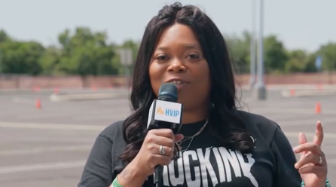 Sharae Moore holds a microphone in front of a driving course, speaking about her experience driving electric trucks