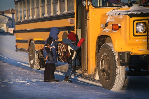 Two children climbing abord a yellow school bus in snowy conditions