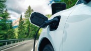 White electric vehicle charging with a road, forest and mountain visible in the foreground