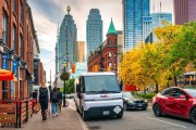 An electric FedEx delivery truck parked at the curb on a Toronto street as pedestrians walk by